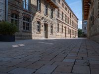 a view of a bricked side walk in an industrial building, with windows on two sides of the walkway