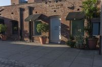 the brick building is next to potted plants and flowers outside the store door with one large plant