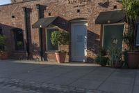 the brick building is next to potted plants and flowers outside the store door with one large plant