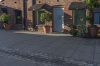 the brick building is next to potted plants and flowers outside the store door with one large plant