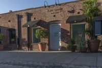 the brick building is next to potted plants and flowers outside the store door with one large plant