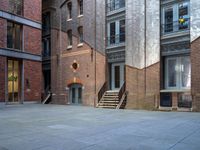 the courtyard is empty of people and steps, with trees in the corner of the building