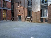 the courtyard is empty of people and steps, with trees in the corner of the building