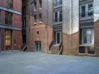 the courtyard is empty of people and steps, with trees in the corner of the building