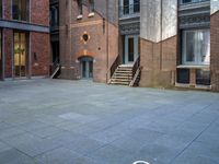 the courtyard is empty of people and steps, with trees in the corner of the building