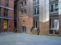 the courtyard is empty of people and steps, with trees in the corner of the building