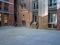 the courtyard is empty of people and steps, with trees in the corner of the building