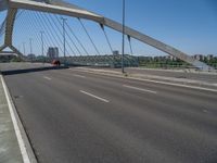 a truck driving across a bridge near a street corner near buildings and a bridge with many cables