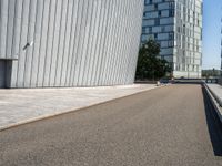 a skateboarder with an open road near large buildings with glass windows on the side