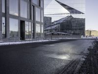 black asphalt road in front of large windows of skyscrapers and glass building with snow on the ground