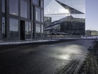 black asphalt road in front of large windows of skyscrapers and glass building with snow on the ground