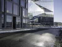 black asphalt road in front of large windows of skyscrapers and glass building with snow on the ground