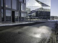 black asphalt road in front of large windows of skyscrapers and glass building with snow on the ground