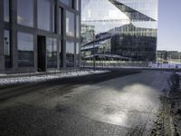 black asphalt road in front of large windows of skyscrapers and glass building with snow on the ground