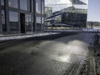 black asphalt road in front of large windows of skyscrapers and glass building with snow on the ground