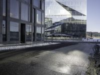 black asphalt road in front of large windows of skyscrapers and glass building with snow on the ground