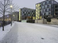 snow has fallen on the ground and trees near the buildings at dusk in front of a bench