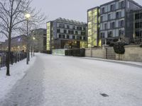 snow has fallen on the ground and trees near the buildings at dusk in front of a bench