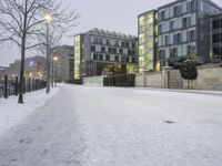 snow has fallen on the ground and trees near the buildings at dusk in front of a bench