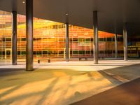 a long bench outside a building with glass windows on the side of the building and trees on the side of it