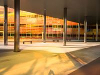 a long bench outside a building with glass windows on the side of the building and trees on the side of it