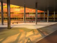 a long bench outside a building with glass windows on the side of the building and trees on the side of it