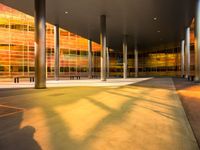 a long bench outside a building with glass windows on the side of the building and trees on the side of it