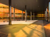 a long bench outside a building with glass windows on the side of the building and trees on the side of it