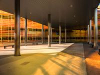 a long bench outside a building with glass windows on the side of the building and trees on the side of it