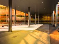 a long bench outside a building with glass windows on the side of the building and trees on the side of it