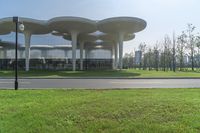 an architecturely designed building that is on the side of the street in front of a field with grass