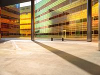 a large building is painted yellow and has glass walls and columns, with a bench outside of it