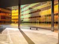 a large building is painted yellow and has glass walls and columns, with a bench outside of it