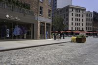 a view of a brick street with shops and patio seatings on either side of it