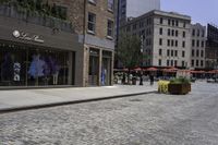 a view of a brick street with shops and patio seatings on either side of it