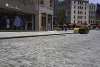 a view of a brick street with shops and patio seatings on either side of it