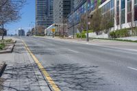 a wide empty city street near many tall buildings and trees in the foreground,