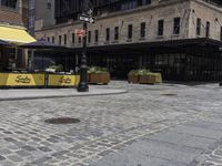 a large building with a yellow awning and a sidewalk corner with chairs and tables