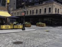 a large building with a yellow awning and a sidewalk corner with chairs and tables