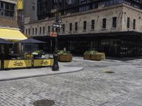 a large building with a yellow awning and a sidewalk corner with chairs and tables