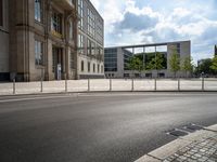 a empty street with a building in the background and a fence around it, leading to the parking lot