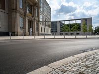 a empty street with a building in the background and a fence around it, leading to the parking lot