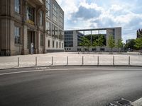 a empty street with a building in the background and a fence around it, leading to the parking lot