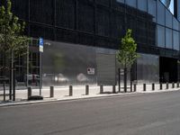 an empty street in front of a large building with glass panels on it and trees