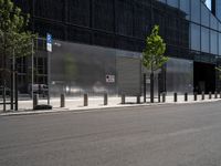 an empty street in front of a large building with glass panels on it and trees