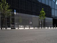 an empty street in front of a large building with glass panels on it and trees