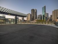 a paved lot with a cityscape in the background at dusk, surrounded by a metal guardrail