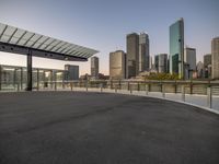 a paved lot with a cityscape in the background at dusk, surrounded by a metal guardrail