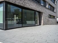 a very narrow path in front of a brick building with large glass doors and a bench in the middle