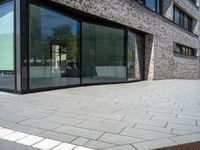 a very narrow path in front of a brick building with large glass doors and a bench in the middle